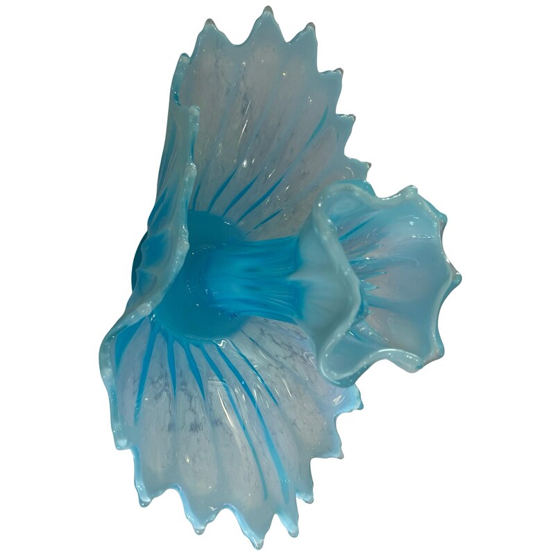 Puede incluir: Una escultura decorativa de vidrio con forma de flor. La escultura presenta una combinaci&oacute;n de colores azul claro y blanco, con detalles en azul oscuro. Los bordes tienen un dise&ntilde;o festoneado, y la forma general recuerda a una flor floreciendo.