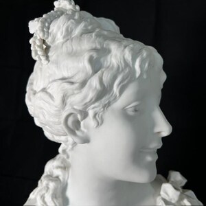 May include: A white porcelain bust of a woman with a detailed hairstyle and a delicate facial expression. The bust is a classic example of fine craftsmanship.