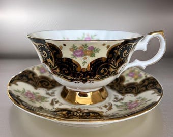 May include: A white teacup and saucer set with a black and gold floral design. The cup and saucer have a delicate, ornate pattern with gold accents.