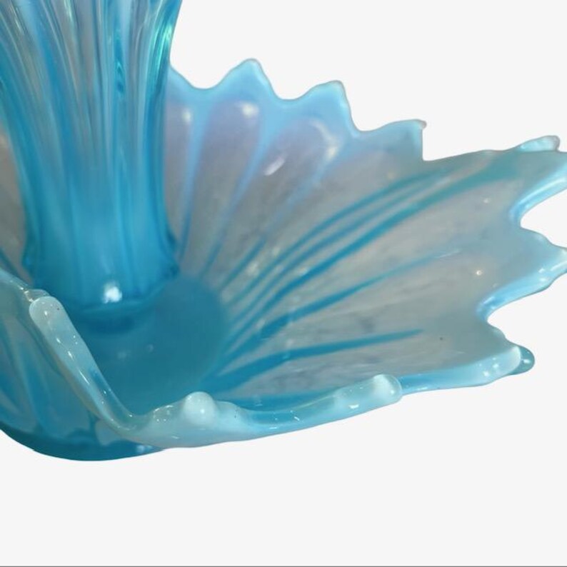 Puede incluir: Primer plano de un cuenco de cristal azul claro con borde festoneado. El cuenco tiene forma de flor con una parte central elevada. El cristal es transl&uacute;cido, con vetas blancas y azules.