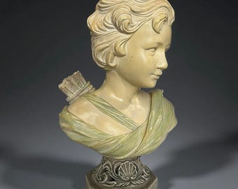May include: A sculpted bust of a young person with curly hair, wearing a draped garment and a quiver of arrows. The bust is in shades of cream and pale green, mounted on a decorative pedestal with a seashell design.