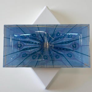 May include: A rectangular, blue glass dish with a floral design in shades of blue and gold. The dish is set on a white, diamond-shaped background. The edges of the dish are outlined in gold.