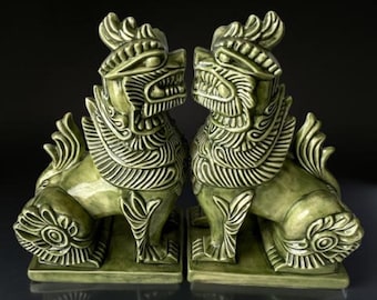 May include: A pair of green ceramic foo dog statues with intricate details. The statues are facing each other and have a traditional Chinese design.