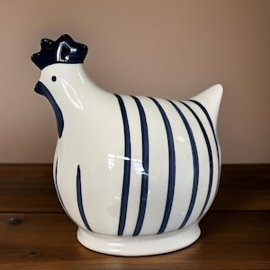 May include: A white ceramic hen figurine with blue stripes. The hen has a black beak and a black comb.