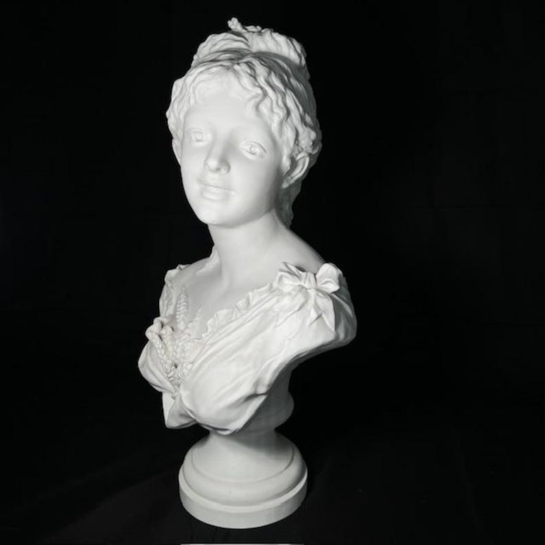 May include: White porcelain bust sculpture of a woman with a detailed hairstyle and a delicate floral design on her dress.
