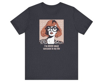 May include: Dark gray t-shirt featuring a pop art style illustration of a woman with red hair, glasses, and the text "I've NEVER faked sarcasm in my life." The woman is wearing a polka dot top.