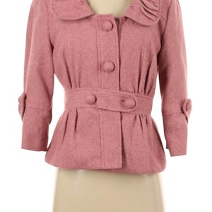 May include: A dusty rose jacket with a rounded collar and three-quarter sleeves. The jacket features a belted waist, three buttons down the front, and decorative buttons on the sleeves. The fabric appears to be a soft, textured material.
