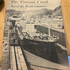 May include: Black and white photograph of a ship, the JACOB VEROLME, navigating the Panama Canal. The image is from a vintage publication titled "The Panama Canal, Funnel for World Commerce."