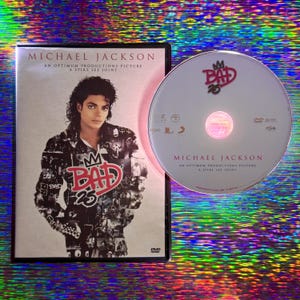 Pode incluir: DVD de "Bad 25" de Michael Jackson. A caixa preta mostra o nome do artista e o título em branco. O disco branco apresenta o logotipo "Bad 25" e o nome do artista.