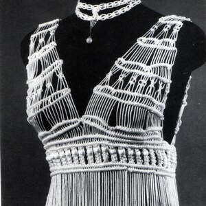 May include: A white macrame dress and matching choker necklace displayed on a mannequin. The dress features a deep V-neck, intricate woven bodice, and a fringed skirt. The choker has a delicate pendant.