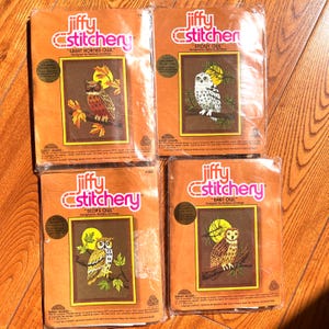 May include: Four Jiffy Stitchery craft kits in plastic packaging, each featuring an owl design by Barbara Jennings: Great Horned Owl, Snowy Owl, Scops Owl, and Barn Owl. Each kit includes a printed design, needle, mounting board, and yarn.