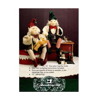 May include: Two seated elf dolls, approximately 19 inches tall, with white hair, red and green hats, and striped stockings. One elf holds a small stuffed animal. The image includes text about easy assembly and placement options.