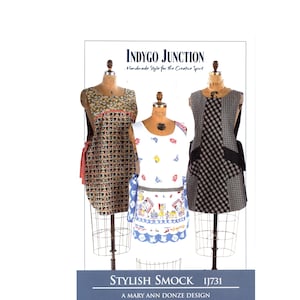 May include: Three aprons on dress forms. The aprons have different patterns: a brown and red grid, a white apron with blue trim and a cartoon design, and a black and white plaid. The text reads "INDYGO JUNCTION" and "STYLISH SMOCK IJ731".