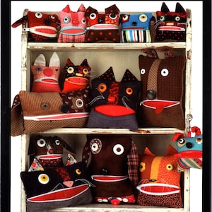 Op de afbeelding: Een verzameling handgemaakte stoffen wezens uitgestald op een witte houten plank. Elk wezen heeft een opvallende ritsmond, knoopogen en diverse textielsoorten met patronen. De tekst luidt INDYGO JUNCTION en ZIPPER CRITTERS IJ850.
