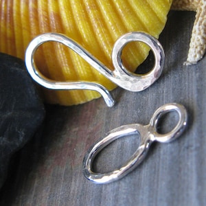 May include: Two silver hammered metal clasps for jewelry making. One clasp is a hook with a loop, the other is a simple loop.