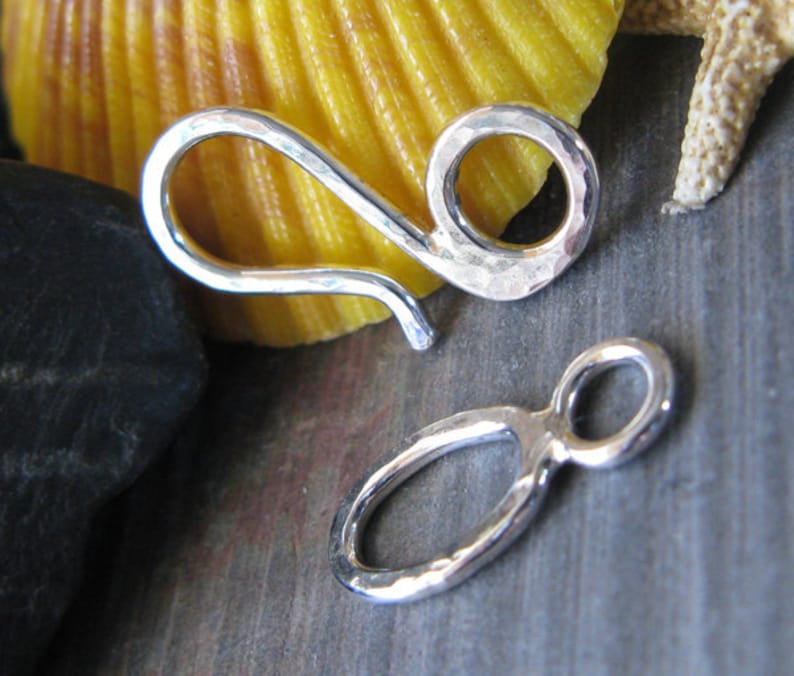 May include: Two silver hammered metal clasps for jewelry making. One clasp is a hook with a loop, the other is a simple loop.