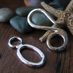 May include: Two silver metal clasps, one is a hook and the other is a loop, both have a hammered texture.