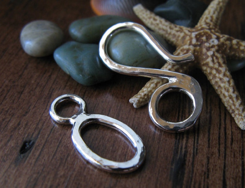 May include: Two silver metal clasps, one is a hook and the other is a loop, both have a hammered texture.