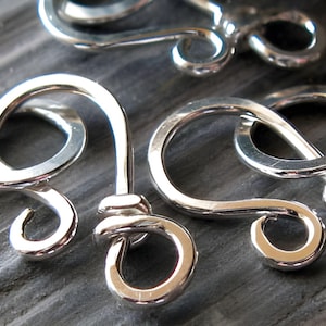 May include: Three silver metal clasps with intricate designs. The clasps are made of smooth, polished metal and have a shiny finish.