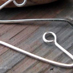 May include: Two silver earring hooks, one with a loop at the end and the other with a straight end. The hooks are on a wooden surface.
