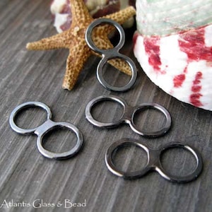 May include: Four black metal double loop connectors. The connectors are in the shape of a figure eight with two circles connected by a bar. The connectors are on a wooden surface.