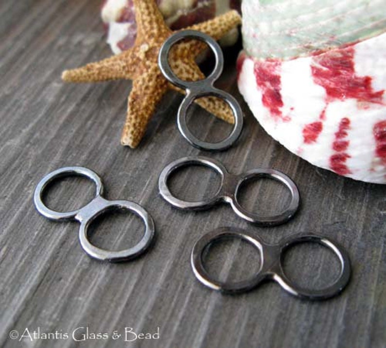 May include: Four black metal double loop connectors. The connectors are in the shape of a figure eight with two circles connected by a bar. The connectors are on a wooden surface.