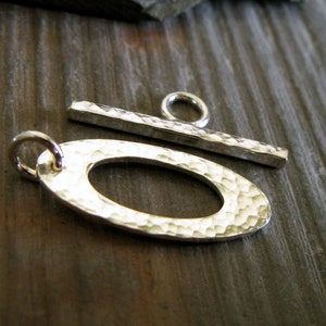 May include: Silver hammered oval toggle clasp with a hammered bar and a ring. The clasp is a jewelry finding for necklaces, bracelets, and other jewelry projects.