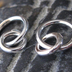 May include: Two silver interlocking rings, each with a smooth, polished finish. The rings are connected in a figure eight shape, creating a unique and modern design.