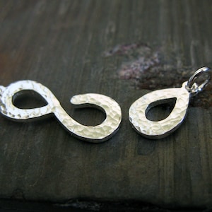 May include: Two silver charms, one shaped like an infinity symbol and the other shaped like a teardrop. Both charms have a hammered texture.