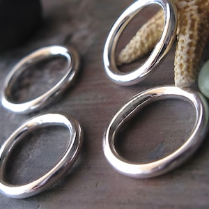 May include: Four silver rings of varying sizes, arranged on a textured surface. The rings are smooth and have a polished finish.
