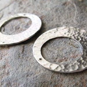 Puede incluir: Dos anillos de metal plateado con textura martillada. Los anillos son redondos y tienen un agujero en el centro.