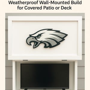 Pode incluir: Um armário de TV exterior de madeira branca com um painel frontal articulado. O armário é montado numa parede e possui um ecrã de TV preto e um logótipo dos Philadelphia Eagles no painel frontal. O texto "DIY Eagles Outdoor TV Cabinet Plan" e "Weatherproof Wall-Mounted Build for Covered Patio or Deck" é apresentado acima do armário. O texto "Printable Woodworking Plan" é apresentado abaixo do armário.
