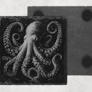 May include: Two square slate coasters. One coaster features a detailed black and white illustration of an octopus with its tentacles spread out. The second coaster is plain grey with black circular pads on the corners. The coasters are designed to protect surfaces from heat and moisture.