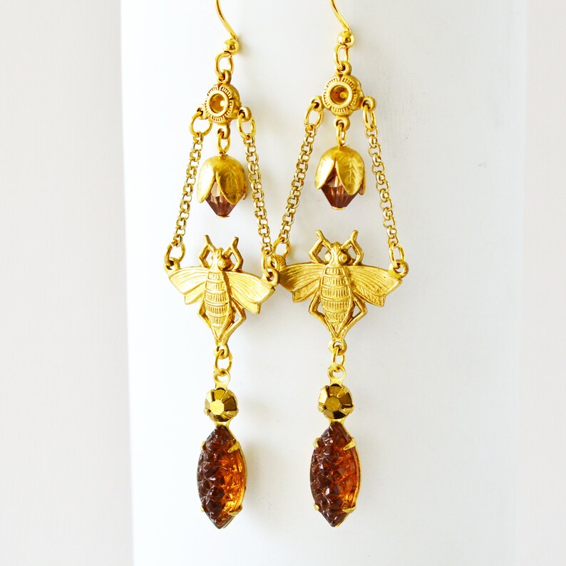 May include: Gold tone earrings with a bee design, amber coloured glass teardrop dangles, and a flower detail.