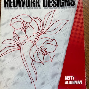 May include: A book titled "Favorite Redwork Designs" features a red floral design on a light gray background. The cover includes the author's name, Betty Alderman, and a red and white checkered pattern.