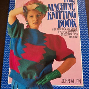 May include: A vintage book cover titled "The Machine Knitting Book" with a pink background and blue border. The cover features a woman wearing a colorful sweater with red, blue, and green accents. The book's subtitle reads "How to Design and Create Beautiful Garments on Your Knitting Machine."