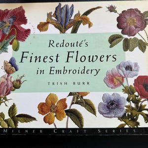 May include: A rectangular book titled Redouté's Finest Flowers in Embroidery by Trish Burr. The cover features a light green central rectangle with black text, surrounded by detailed embroidered illustrations of red, blue, yellow, and pink flowers.
