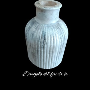 Può includere: Un vaso in ceramica bianca con una texture a coste e una lavata grigia. Il vaso è vuoto e ha una forma arrotondata.