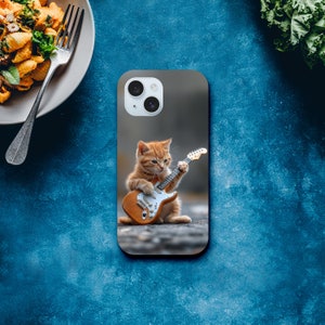 May include: A phone case with a cute orange tabby kitten playing an electric guitar. The case is gray and has a white camera lens.