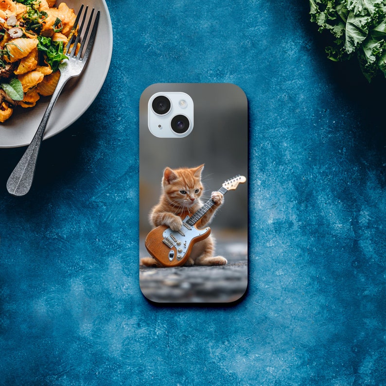 May include: A phone case with a cute orange tabby kitten playing an electric guitar. The case is gray and has a white camera lens.