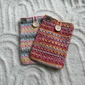 May include: Two rectangular crochet pouches featuring variegated yarn in shades of pink, orange, yellow, and grey. Each pouch has a wooden button closure with the text Handmade with love and a small brown fabric tag labeled Berry Crafty Studio.