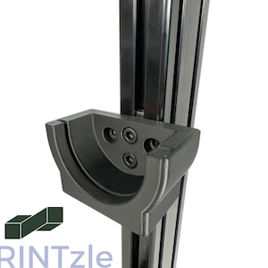 Könnte beinhalten: Eine schwarze, 3D-gedruckte Halterung aus Kunststoff mit drei Schraubenlöchern, montiert an einer schwarzen Metallschiene.