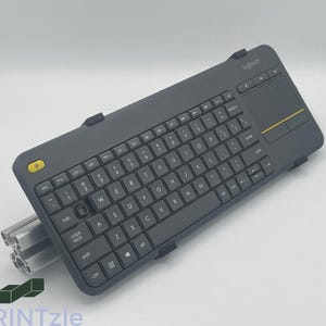 May include: A black wireless keyboard with a built-in touchpad and a yellow button. The keyboard has a Logitech logo on the top right corner.