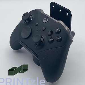 Op de afbeelding: Een zwarte Xbox-controller met een textuur grip en een zwarte standaard. De controller heeft een zwart en zilver ontwerp met een zwarte knop aan de bovenkant.