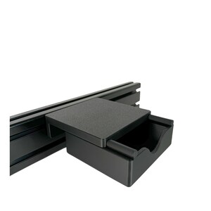 May include: A black drawer with a lid that can be used to store small items. The drawer is mounted on a black metal track.