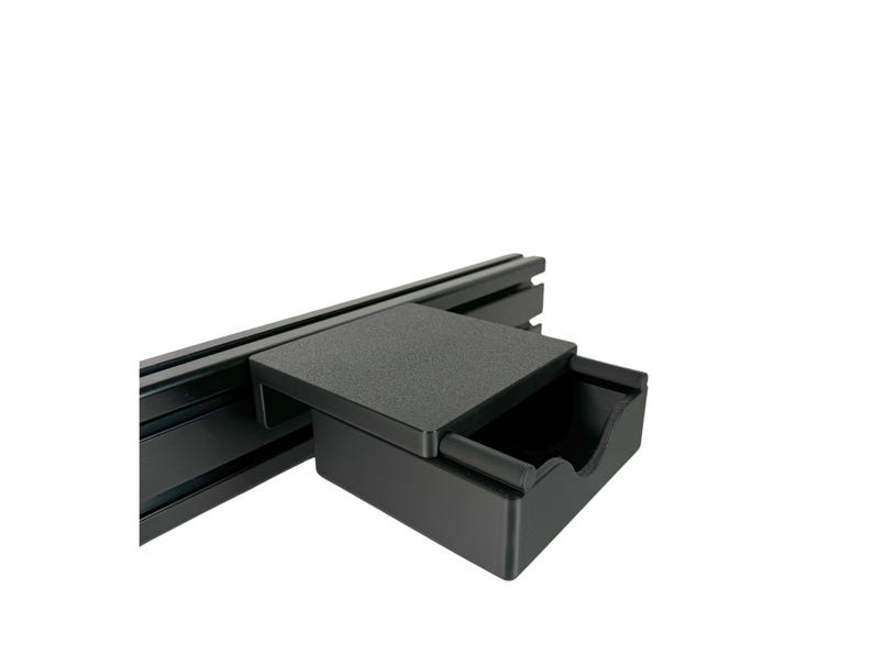 May include: A black drawer with a lid that can be used to store small items. The drawer is mounted on a black metal track.