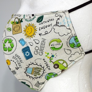 K&ouml;nnte beinhalten: Eine wei&szlig;e Gesichtsmaske mit schwarzen elastischen Ohrschlaufen. Die Maske ist mit einem gr&uuml;nen, blauen und gelben Kritzelmuster verziert, das die W&ouml;rter "Go Green", "Natural Energy", "Energy Efficient", "Re-use", "Home Sweet Home" und "Oxygen" enth&auml;lt.