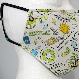 K&ouml;nnte beinhalten: Eine wei&szlig;e Gesichtsmaske mit schwarzen verstellbaren B&auml;ndern. Die Maske hat einen gr&uuml;nen und blauen Druck mit den Worten "Recycle", "Sustainable", "Environmental Conscious" und "Eco Friendly".