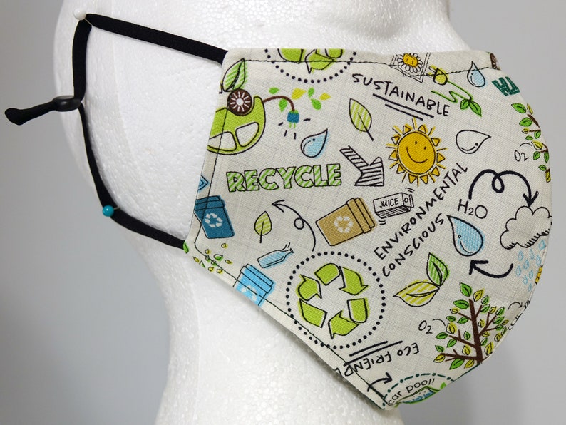 K&ouml;nnte beinhalten: Eine wei&szlig;e Gesichtsmaske mit schwarzen verstellbaren B&auml;ndern. Die Maske hat einen gr&uuml;nen und blauen Druck mit den Worten "Recycle", "Sustainable", "Environmental Conscious" und "Eco Friendly".