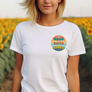 Könnte beinhalten: Weißes T-Shirt mit einer Grafik im Retro-Stil, auf dem "Good Data Vibes" mit einem Datenbanksymbol steht. Die Grafik befindet sich auf einem Kreis mit einem sonnenuntergangsartigen Hintergrund.
